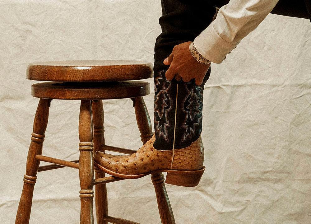 A man resting his foot on a stool and wearing Tony Lama Boots